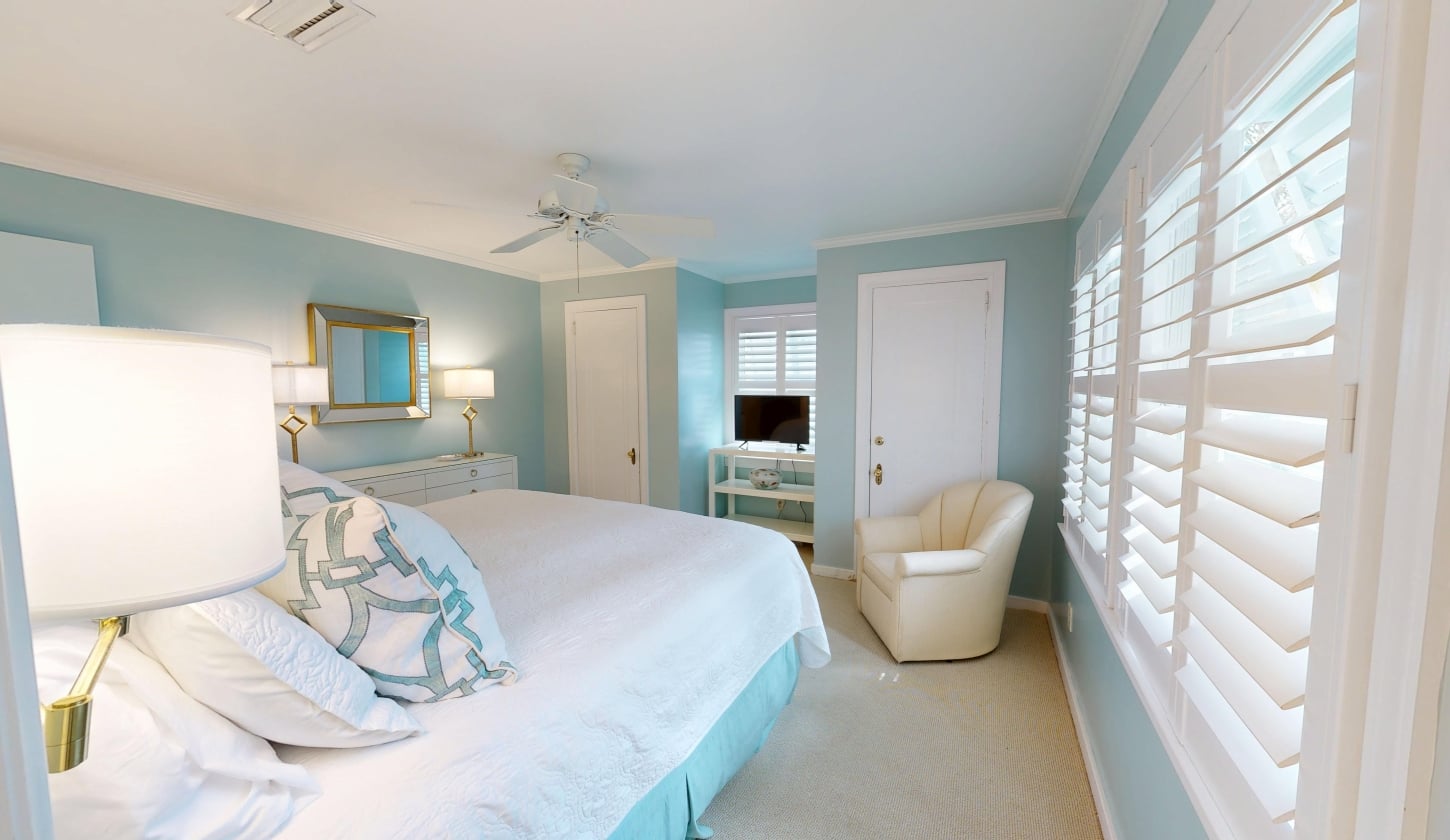 A soft blue bedroom with a cozy white chair beside the bed