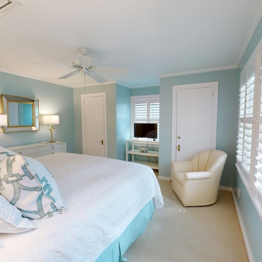 A soft blue bedroom with a cozy white chair beside the bed