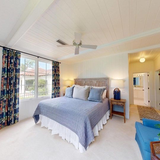 A large bed with big windows and a ceiling fan