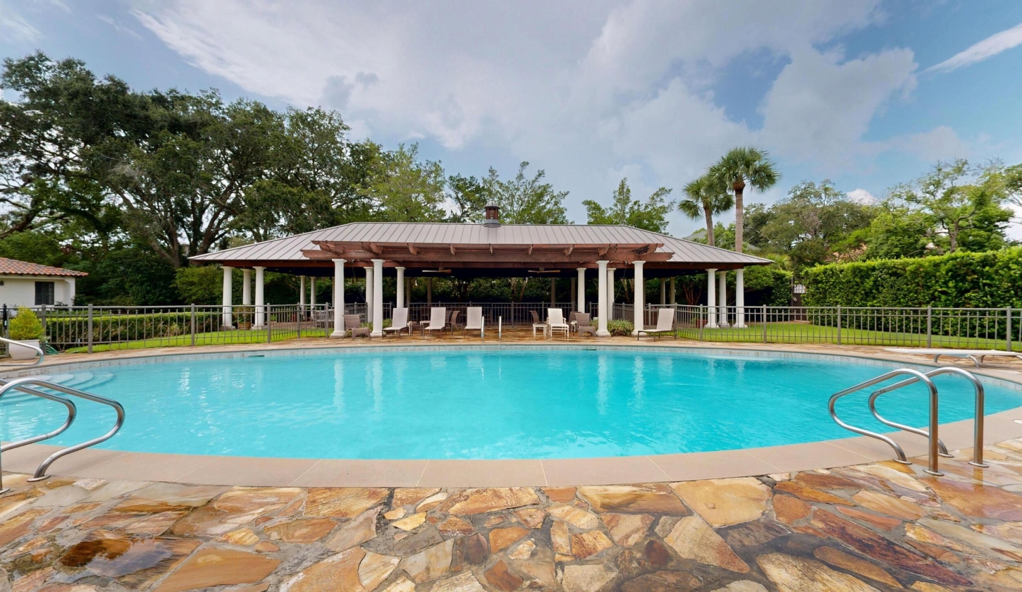 A long pool with a covered patio and lounge chairs in the background