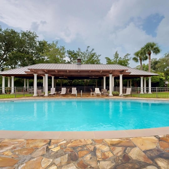 A long pool with a covered patio and lounge chairs in the background