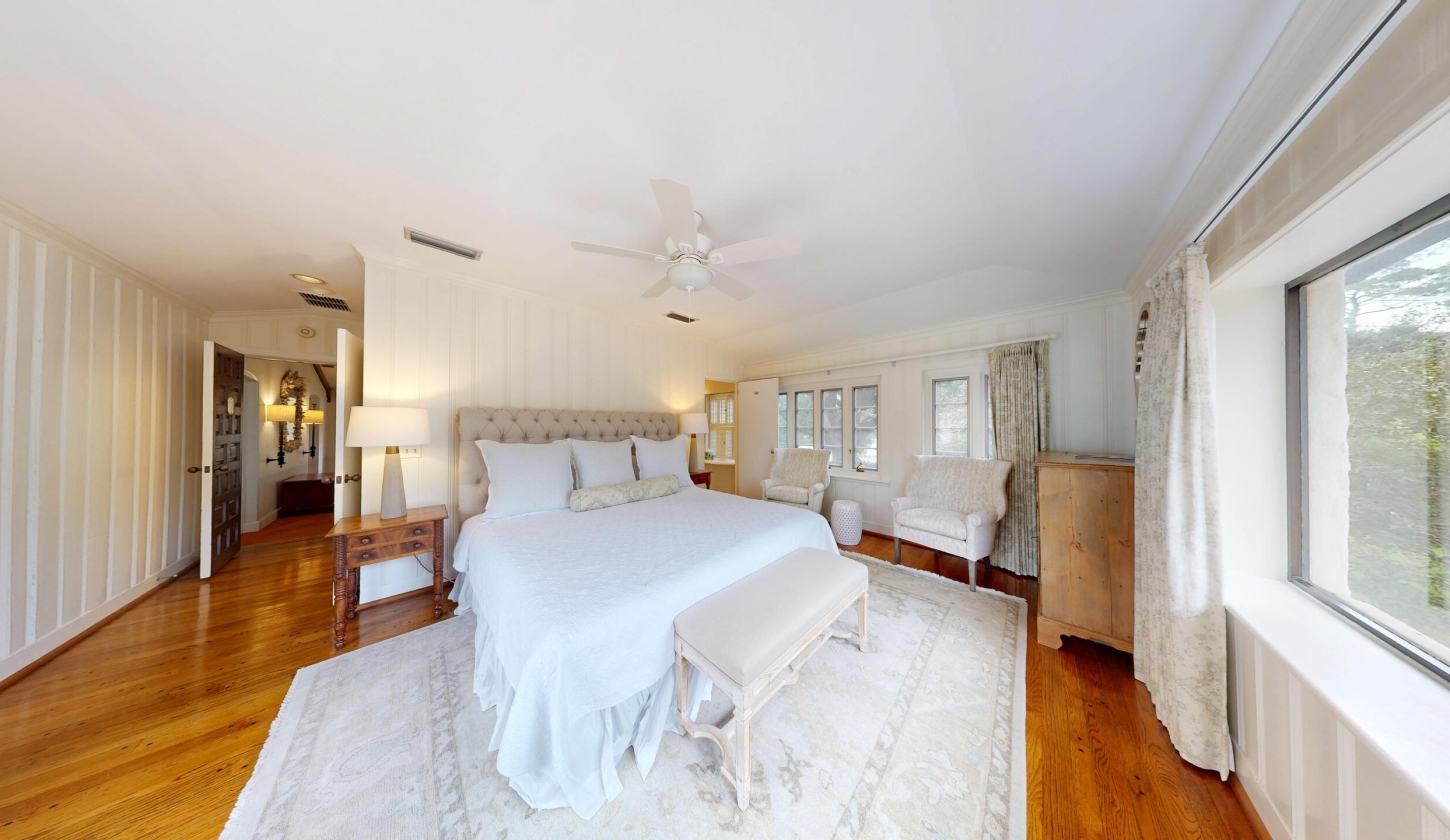 A primary bedroom with white sheets and hardwood floors