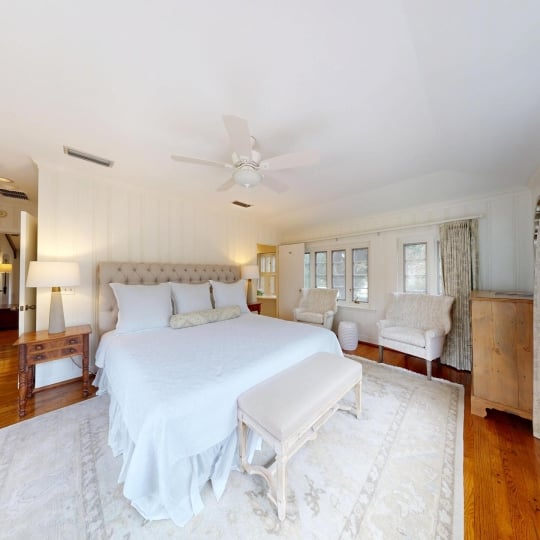 A primary bedroom with white sheets and hardwood floors