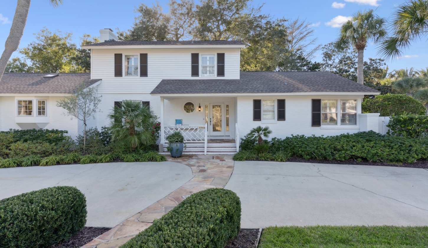 Front of a cottage with white siding and greenery