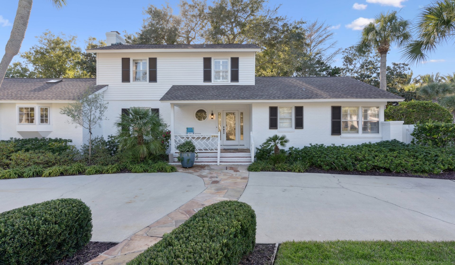 Front of a cottage with white siding and greenery