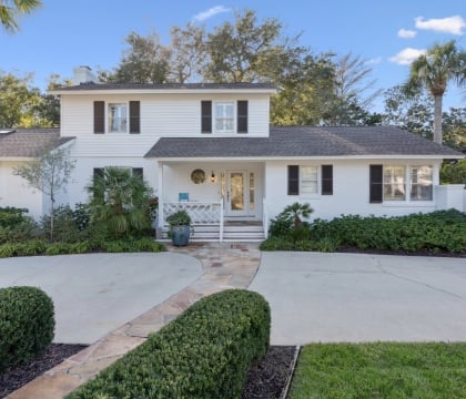 Front of a cottage with white siding and greenery