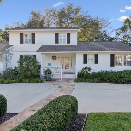 Front of a cottage with white siding and greenery