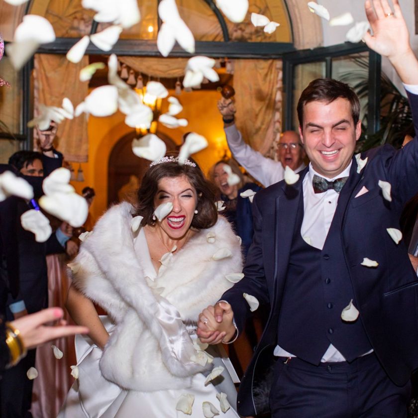 bride and groom leaving while flower petals are thrown at them