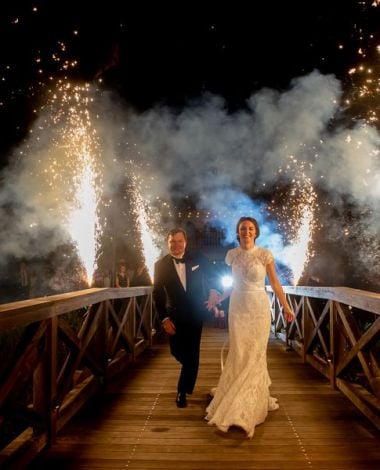 bride and groom walking over bridge with fireworks going off behind them