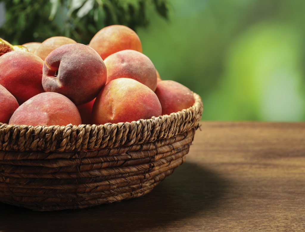 Many whole fresh ripe peaches in basket on wooden table against blurred background, closeup. Space for text