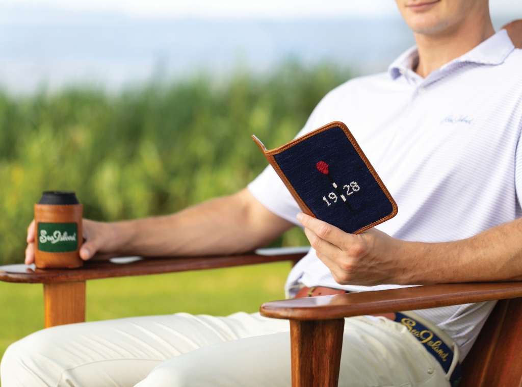 A man sitting on an armchair holding his phone in a needlepoint case