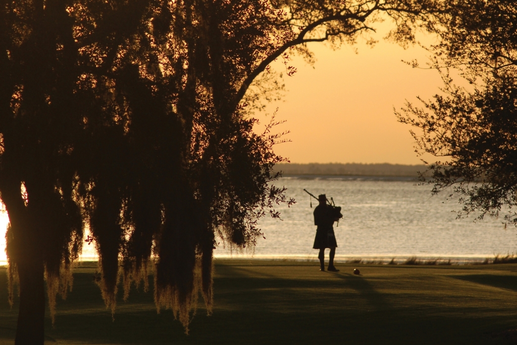 Silhouette of a bagpiper playing by a lake at dusk