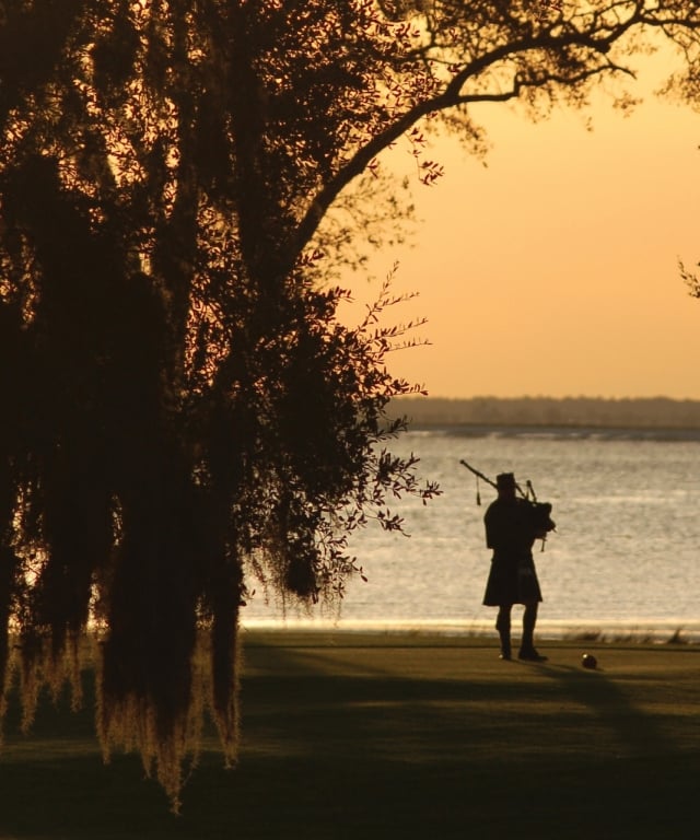 Silhouette of a bagpiper playing by a lake at dusk