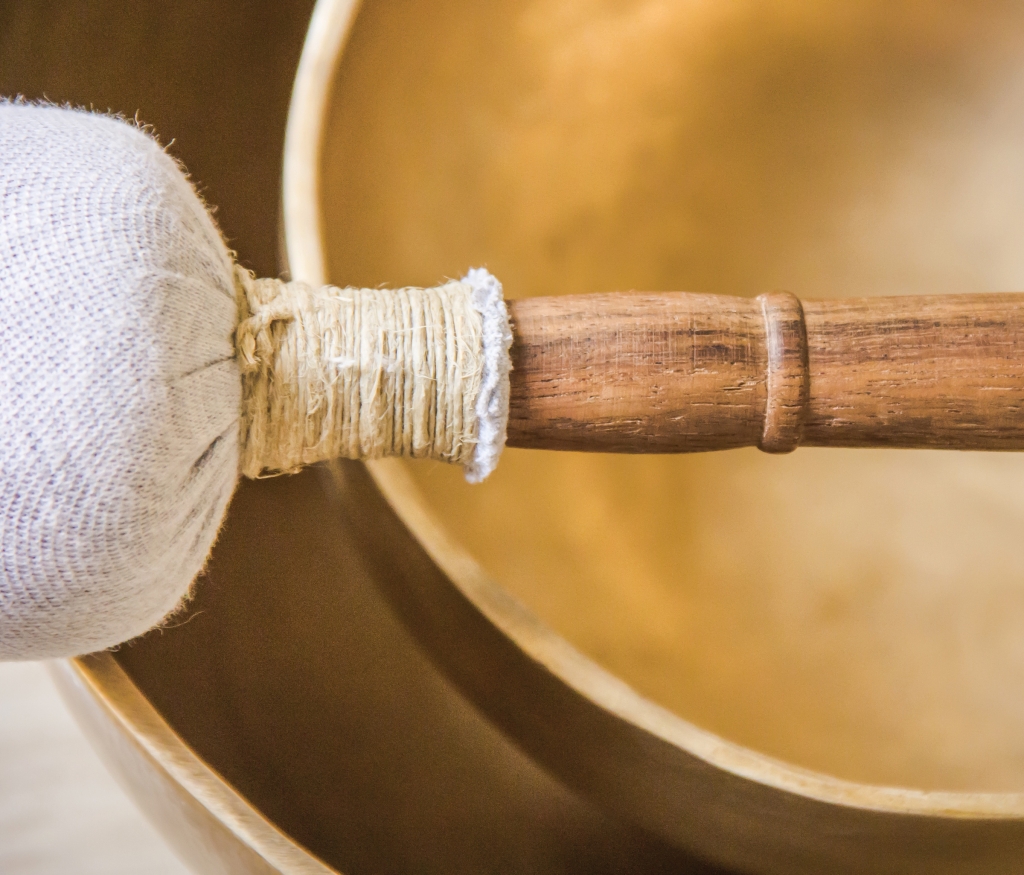 A closeup of two golden round singing bowls and a wooden struck on the table