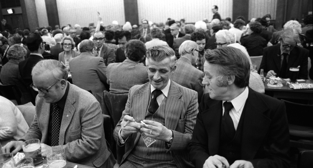 Men playing Bingo UK 1980S. Coventry Working Mens Club, Saturday night bingo evening entertainment. All dressed up and looking smart, two men friends chatting and smoking. Coventry, England circa 1981.