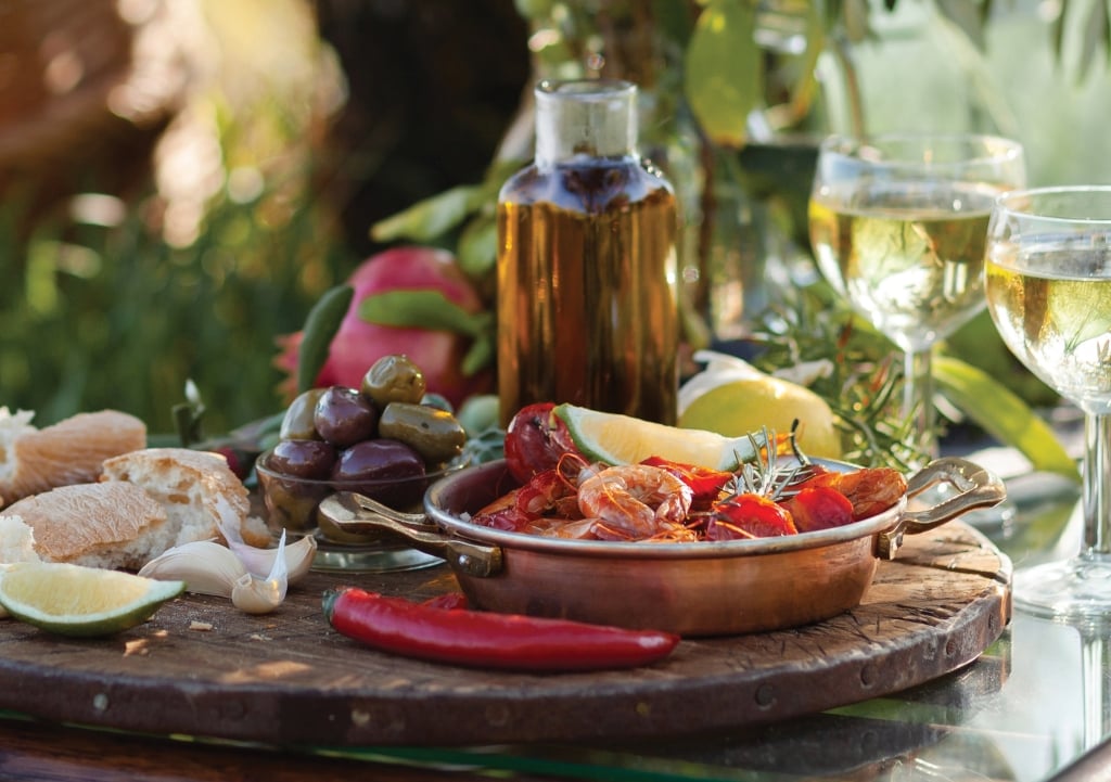 Romantic italian lunch outside of a couple: copper pan with delicious and spicy fried shrimps with herbs and garlic, bottle of olive oil, wine, bread. Luxury lifestyle, gourmet food. Banner