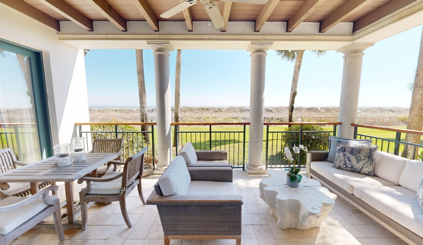 A patio with ample seating looks out towards green grass and water