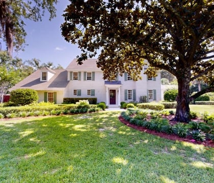 A green lawn with trees and a large white cottage